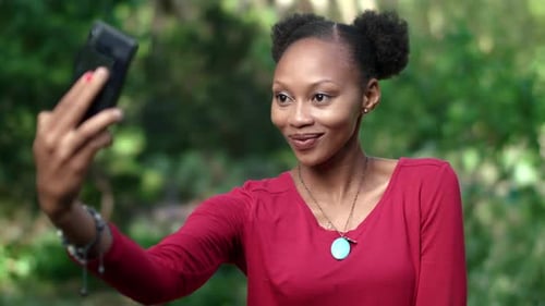 4k Video footage of a young woman sitting on a bench in a park taking selfies with her cellphone
