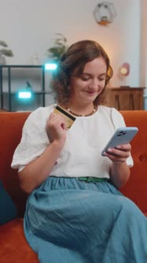 Happy Young Woman Using Credit Bank Card and Smartphone While Shopping Online Sitting on Sofa Couch