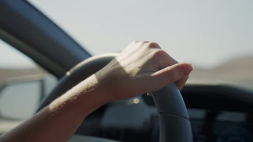 Close up on female hand on steering wheel driving on desert highway with one hand on wheel. Relaxed