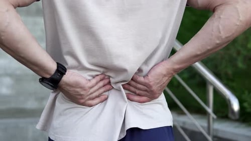 A man feels a sharp pain in his lower back and massages his back during exercise.