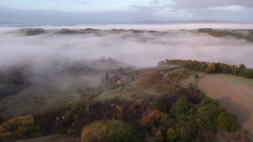 Tuscany valley filled with mist in morning, small rural farm house, aerial