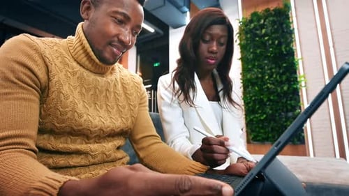 Black male and female workers in an office discussing business using a tablet. Slow motion