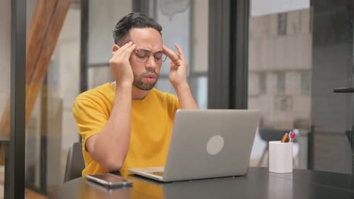 Stressed Young Adult Massaging Temples at Desk