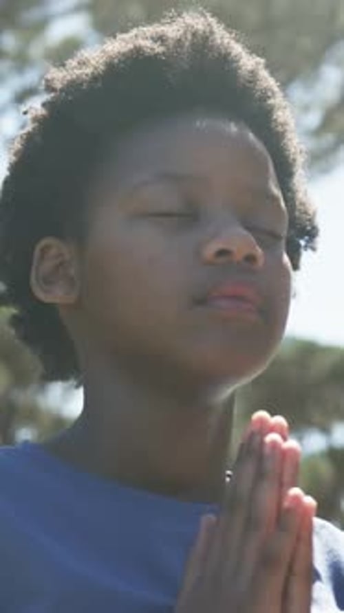 Vertical video: Eyes closing starting teen holding hands pressed praying at park blue top curls