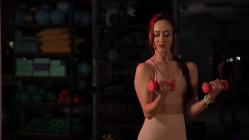 Athletic Woman Doing Bicep Curls with Dumbbells in the Gym