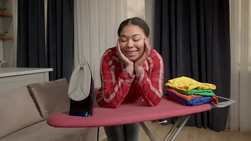 Woman Resting on Ironing Board with Folded Clothes