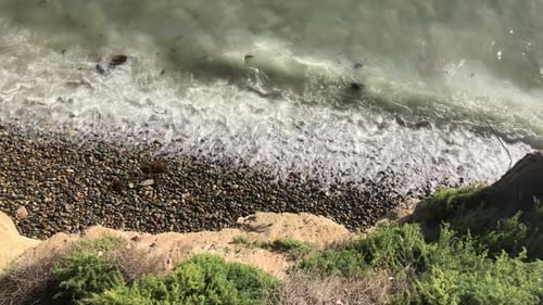 Clip in Zeitlupe. Meereswellen bei Tageslicht am Strand. Neige dich hoch, Wellen kommen mit Algen herein und treffen auf den Stopp