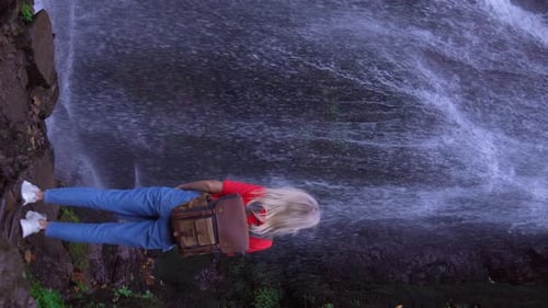 Back view of young woman standing in front of waterfall.