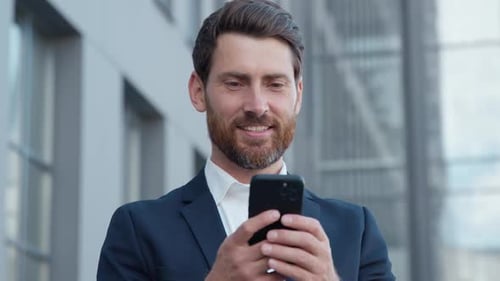 Smiling Caucasian Happy Business Man with Mobile Phone Browsing Social Network in City Businessman