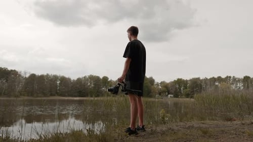 Young man standing in nature holding gimbal with camera for filmmaking