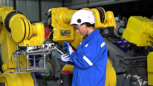 Une
technicienne programme un bras robotique avec une tablette numérique et un robot d'assemblage dans une usine. Appren