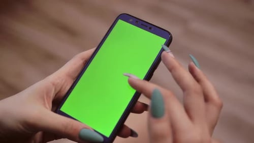 girl with long nails holds a phone with a green screen. woman with beautiful manicure swipes her fin