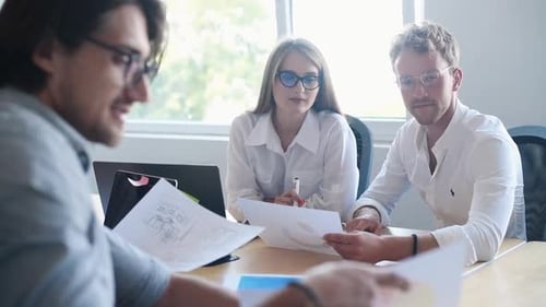 Young business people in formal clothes sitting by the table and working in the office with document