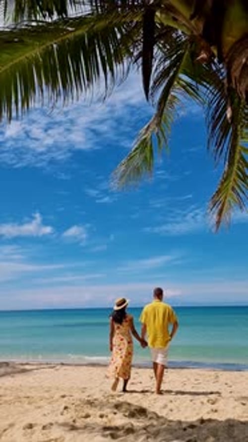 a Mature Couple Walking on a Tropical White Sandy Beach with Palm Trees in Thailand