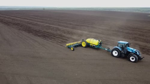 Blue tractor with yellow seeder working on the field in Ukraine OA