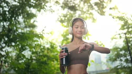 Woman with Headphones and Water Bottle in Park