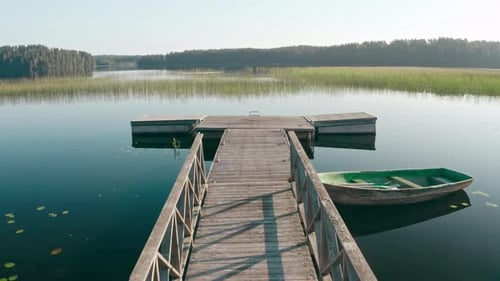 Drone Flies Over Wooden Old Boat Moored at Pier on Large Lake Among Forest
