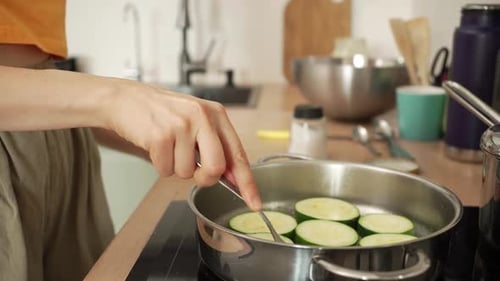 Female Hands Using a Fork to Turn Over Delicious Sliced Zucchini Frying in a Stainless Steel Pan on