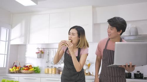 Young Couple Enjoys Sandwich and Laptop in Kitchen