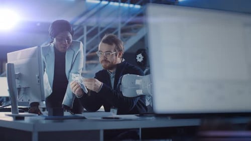Entwicklungsingenieur für Elektronik arbeitet an seinem Schreibtisch, spricht mit dem Projektmanager, zeigt High-Tech-P