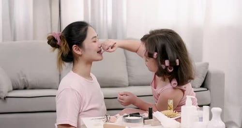Kleines gemischtrassiges Mädchen hält selbstbewusst den Pinsel, während sie weiterhin Make-up auf die asiatische Mutter aufträgt
