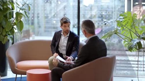 Two talking businessmen sitting in office lounge
