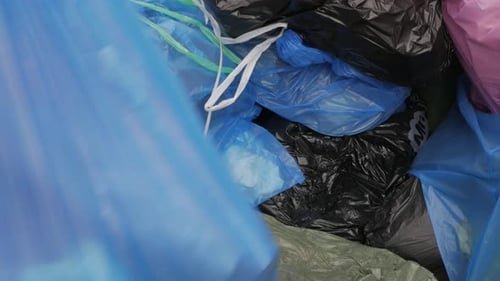 Se arroja una bolsa llena de basura encima de una pila grande de bolsas de basura.