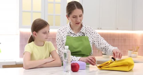 Woman packing lunch bag for her daughter at table in kitchen