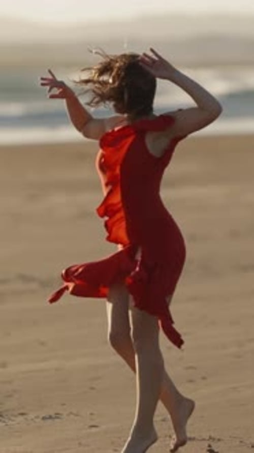 A Young Woman in Red Dress Dancing on Sandy Beach