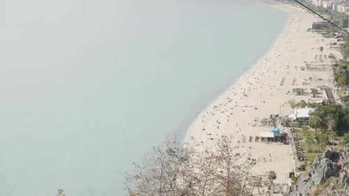 Flying down the mountain through the trees. The beach and the sea are below. People are resting.