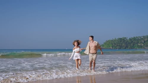 Attractive Couple Run Holding Hands in Sea Surf Waves Tanned Man and Woman Having Fun on Summer
