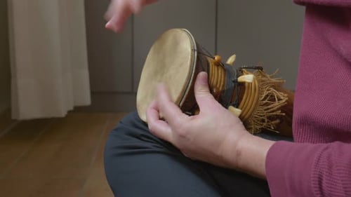 Hands Playing a Small Percussion Instrument Decorated with African Motifs