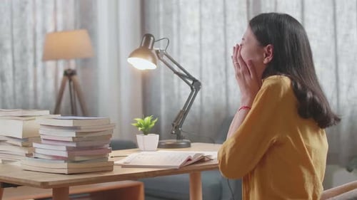 Side View Of Young Asian Female Studying At Home Yawning And Sleeping While Reading Books