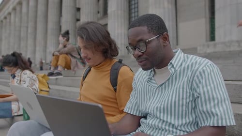 Two Students Discussing Homework and Using Laptops Outside the University