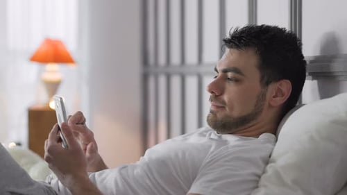 Man Using Smartphone While Relaxing in Bed