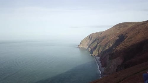 Couple Sat on Cliff Edge Overlooking Ocean, Drone Shot Dolly Forward