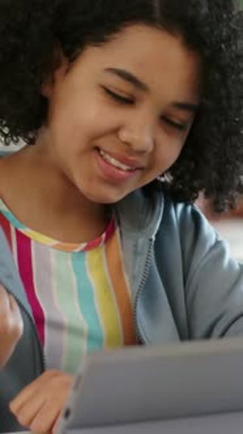 Vertical video: Reacting to assignment, student in hoodie tapping tablet with stylus in classroom