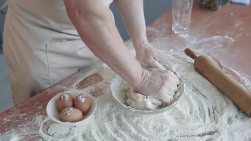 The cook in the bakery kneads the dough with his hands and begins to prepare bread.