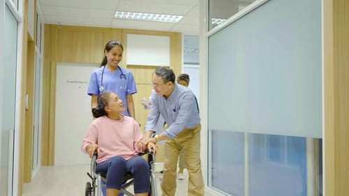 Front view of nurse pushing wheelchair with female senior patient in hospital corridor.