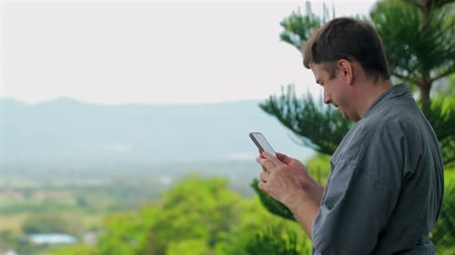 Man Standing Outdoors on Sunny Day Holding Smartphone and Smiling