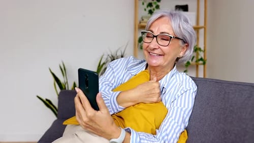 Happy Senior Woman Using Mobile Phone While Relaxing at Home