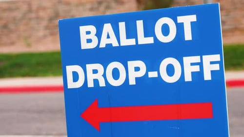 Blue Ellection Ballot Drop-off Sign with Red Arrow Pointing Left and Blowing in the Wind Outside