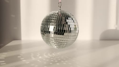 Disco ball rotates on a white background with shadows and casts rays of bright light.