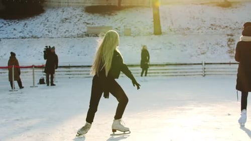 A Young Blonde Woman Skating on the Ice Rink Outdoors