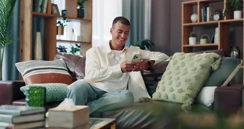 Smiling Young Adult Using Smartphone on Couch at Home