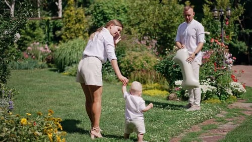 Rear view of a woman leading her little baby by the hand outdoors.