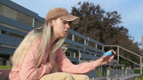 Young Woman Uses Inhaler on Stadium Seats