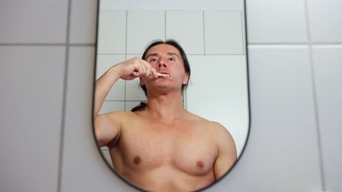 Man Brushing Teeth Looking in Bathroom Mirror