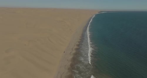 Aerial view of sand dune, ocean, and vehicle at Sandwich harbour, Namibia.