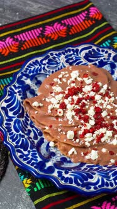 Vidéo verticale, enfrijoladas mexicaines, tortillas plates à la sauce aux haricots avec chorizo émietté sur le dessus